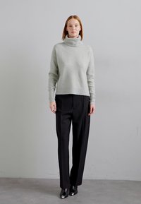 Maglione grigio chiaro a collo alto realizzato in materiale morbido, abbinato a pantaloni neri a vita alta. I pantaloni hanno una vestibilità dritta e un design minimal.