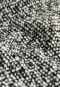 Tissu textile avec un motif tissé texturé en noir et blanc, affichant une surface douce et duveteuse avec des éclats contrastants.