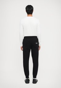 Sorte sweatpants med smal passform, med elastisk midjebånd og baklomme. En hvit logo er synlig på lommen.