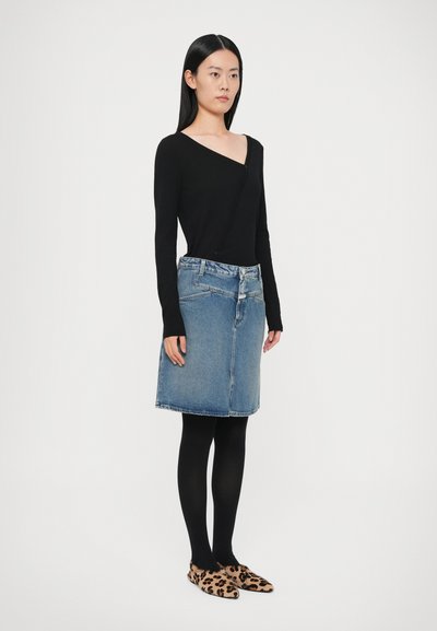 Black long-sleeve top with a v-neck, blue denim skirt with pockets, black tights, and leopard print slip-on shoes.
