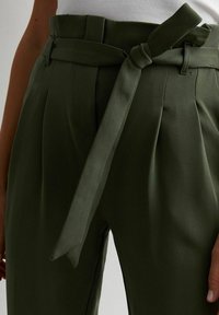 Pantaloni a vita alta verde oliva con pieghe e una cintura in tessuto annodata in vita.