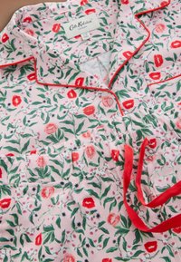 Floral pajama set in light pink with red and green floral patterns. Features a collared design, red piping, and elastic waistband.