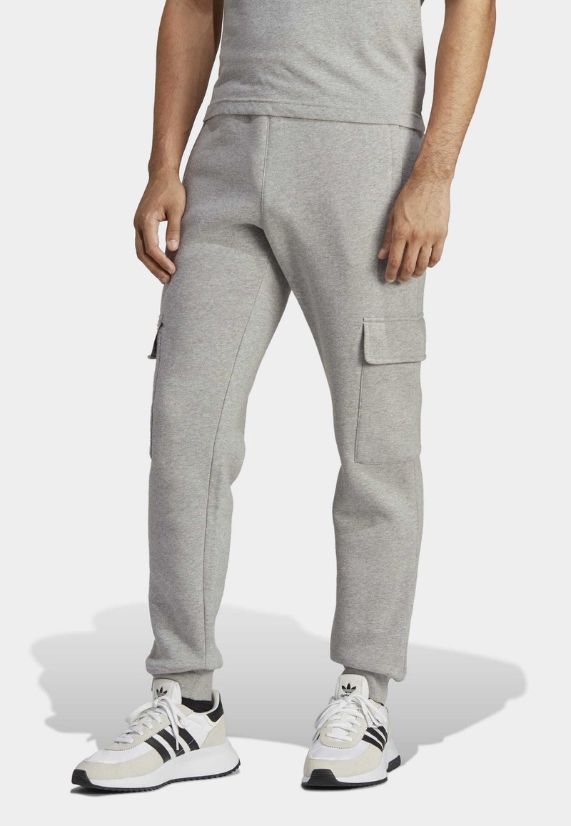Pantalons de survêtement gris en mélange de coton, dotés de poches cargo latérales et de jambes fuselées. Portés avec des baskets blanches et un t-shirt gris.