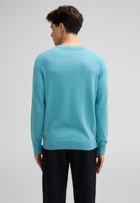 Türkiser Pullover mit gerippten Bündchen und Saum, mit einem Rundhalsausschnitt und Raglansleevs. Der Stoff wirkt weich und hat eine melierte Textur.