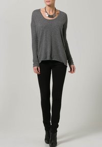 Pull gris à manches longues avec un col arrondi, associé à un pantalon noir ajusté. Complété par des bottines noires et un collier métallique épais.