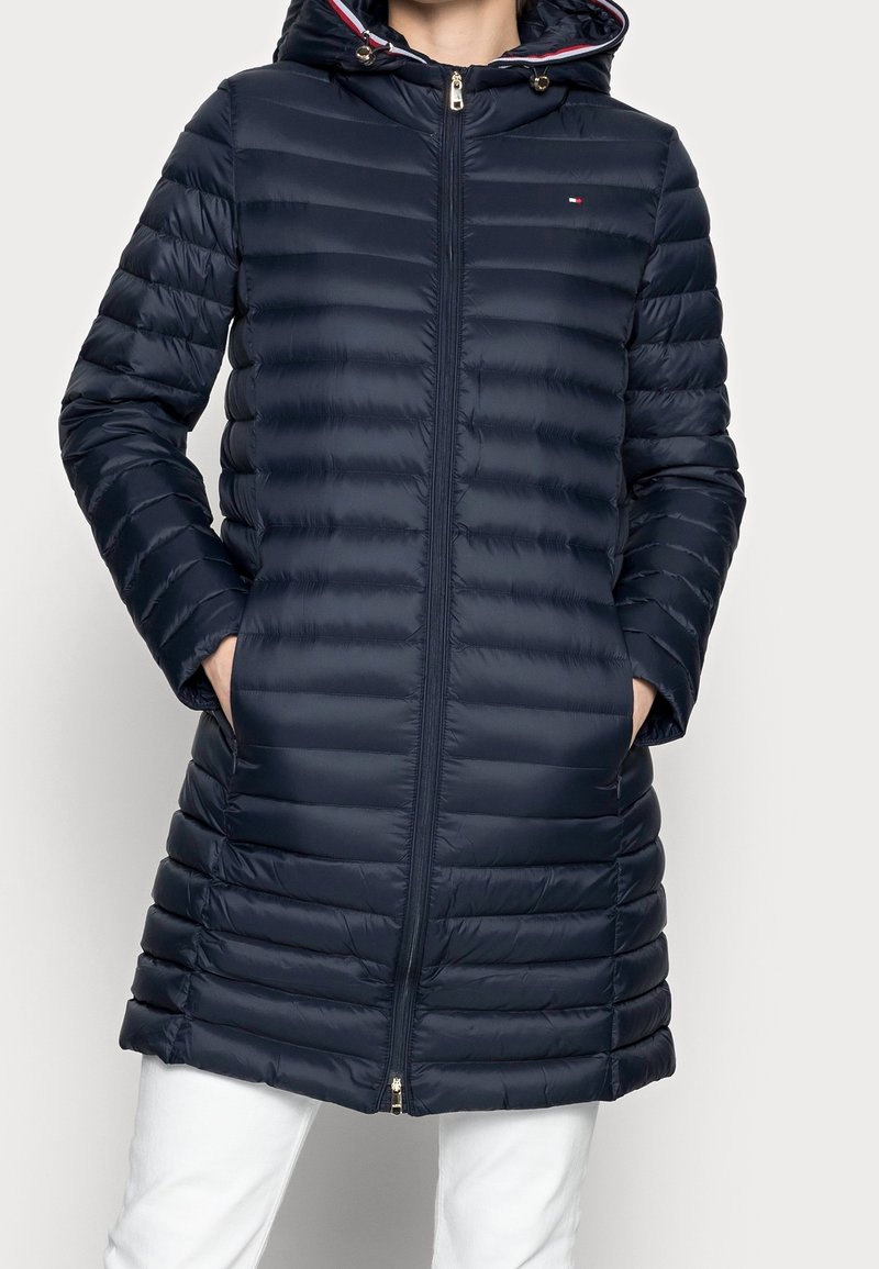 Námorní puffer jacket s vodorovným prošíváním, kapucí, zipovým uzávěrem a bočními kapsami; má kontrastní barevné akcenty v podšívce.