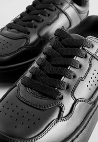 Svarta lädersneakers med texturerad yta, platta svarta snören, perforerat tåkåpa och kontrasterande sömnadsdetaljer.