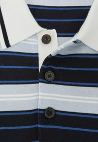 Zbliżenie na prążkowaną dzianinową koszulkę polo z białym kołnierzem i trzema czarnymi guzikami, z poziomymi paskami w kolorach granatowym, niebieskim, jasnoniebieskim i białym.