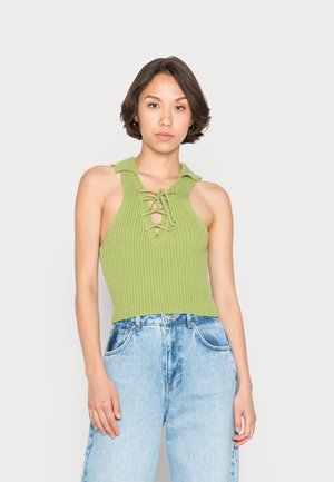 Top crop verde com nervuras e gola, apresentando uma frente com cordão. Combinado com jeans de ganga claros de cintura alta.