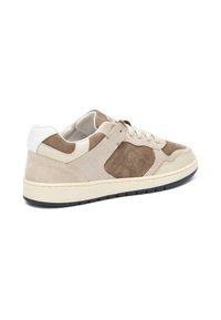 Zapatillas de ante beige y marrón con un talón blanco, cordones crema y una suela de goma texturizada. Presenta detalles perforados y acentos en contraste.