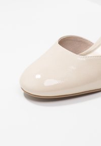 Béžová lakovaná plochá obuv s kulatou špičkou, hladkým povrchem a minimalistickým designem. Interiér má světlou podšívku a měkký povrch.