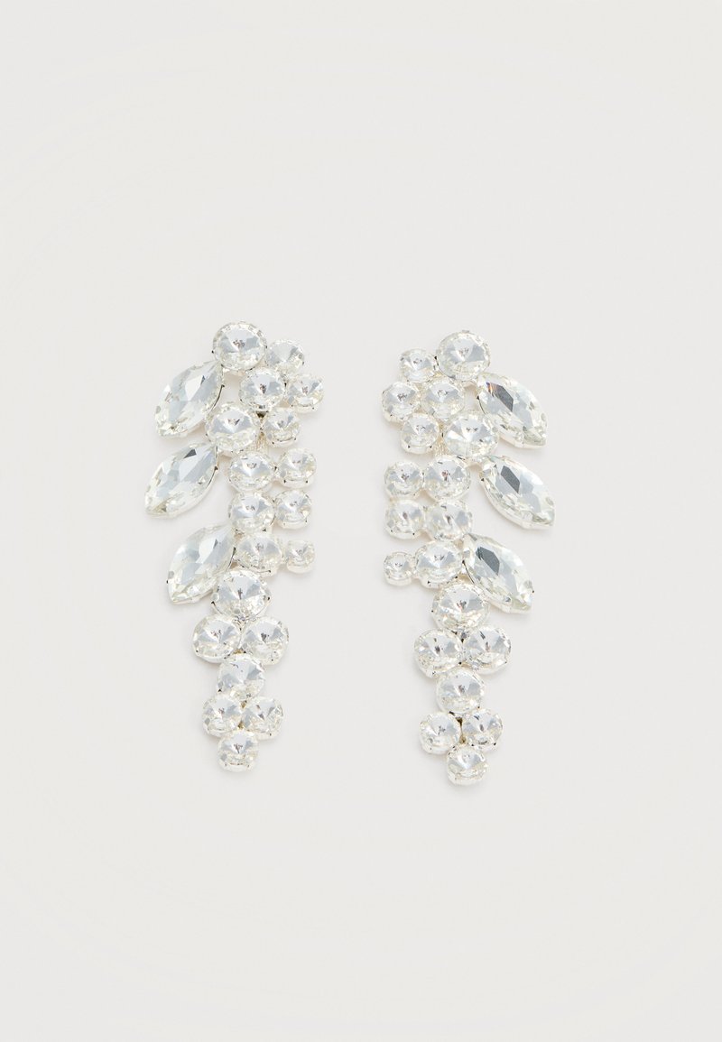 Ζευγάρι σκουλαρίκια σε ασημένια απόχρωση με συσσωρευμένους διαφανείς γυαλισμένους κρυστάλλους σε στρογγυλά και λοξοτομημένα σχήματα σε λευκό φόντο.