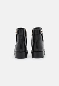 Botas de tobillo de cuero negro con una textura suave, punta redondeada y tacón cuadrado. Presentan una cremallera lateral y acentos de hebilla metálica.