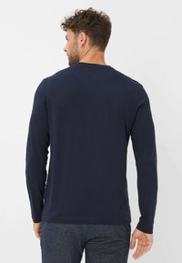 Marineblaues Langarmhemd aus weichem Stoff, mit rundem Halsauschnitt und bequemer Passform. Es hat minimalistische Nähte und ein kleines Etikett am Saum.