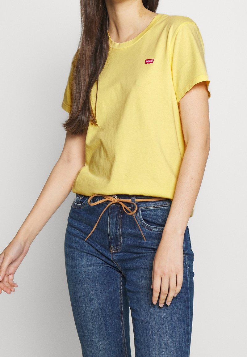 Žluté bavlněné tričko s kulatým výstřihem a krátkými rukávy. Na hrudi je malé červené logo Levi's. V kombinaci s modrými džínami.