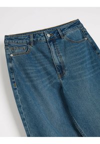 Jeans denimowe w średnim odcieniu niebieskiego, z klasycznym pięciopocketowym wzornictwem, widocznymi szwami oraz zapięciem na guzik w talii.