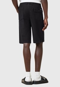 Black shorts made of lightweight fabric, featuring two back pockets and a button closure. Worn with black sandals and white socks.