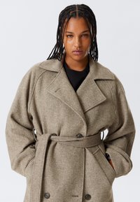 Beige mantel van een wolblend met een double-breasted ontwerp, brede revers, ceintuur in de taille en diepe zakken met een getextureerde afwerking.