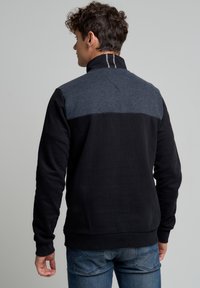 Maglione nero con un vivagno grigio scuro e un colletto alto. Presenta polsini e orlo a coste, tessuto testurizzato e dettagli di cucitura sottili.