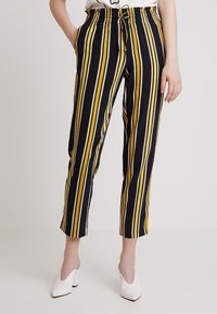 Svarta och gula randiga byxor med resårmidja, kort längd och snörningsdetalj. Kombination med vita klackskor.