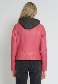 Lyserød l æderjakke med en grå hætte, ribbet tekstur i kanten og tætsiddende design med sømdetaljer på ryggen.