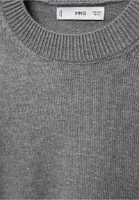 Col de pull en maille côtelée grise avec étiquette de taille MNG indiquant EUR-USA S, MEX CH.