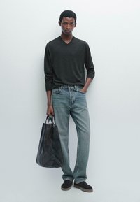 Schwarzer V-Ausschnitt-Pullover, hellblaue Jeans und dunkle Tragetasche; das Modell trägt dunkle Schuhe. Das Outfit zeichnet sich durch eine lockere Passform und ein minimalistisches Design aus.