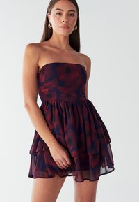 Strapless bloemenjurk met een gelaagde rok met rode en donkerblauwe patronen, gemaakt van lichtgewicht, transparante stof.