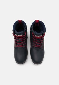 Paire de bottes noires Levi's avec des lacets rouges et une doublure bleu marine, vues de dessus sur fond blanc.