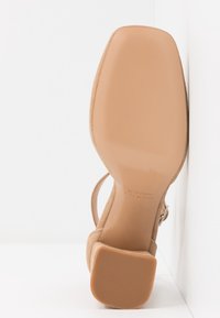 Sandale beige en daim à talon haut avec un bout carré et un talon bloc, semelle marquée de la taille 37 et "Fabriqué en Italie."