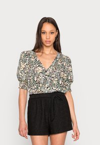 Blusa com estampado floral, mangas bufantes, decote em V e fundo preto. Combinada com calções pretos de cintura alta com cinto de laço.