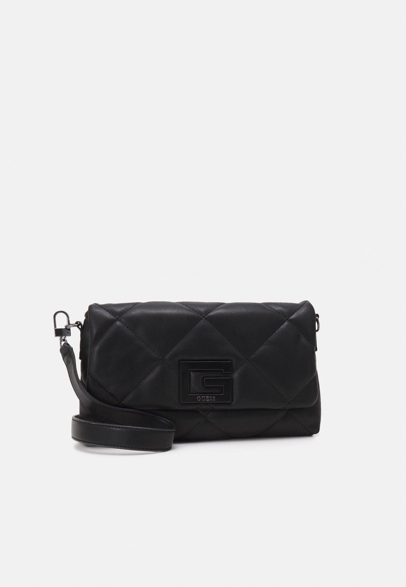 Sac bandoulière matelassé noir avec grand logo G Guess embossé à l'avant, fermeture à rabat et bandoulière amovible sur fond blanc.