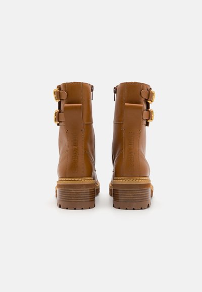 Brown leather ankle boots with two gold buckle accents, textured heel, side zipper, and stitched detailing on the back.