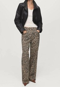 Veste en cuir noire, débardeur blanc et pantalon beige taille haute avec un imprimé léopard noir. Les chaussures sont pointues avec une teinte marron.