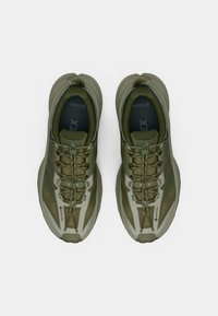 Olivengrønne treningssko med strukturert overdel, forsterket tåhette og Gore-Tex-logo. Har rask snøresystem og polstret såle.