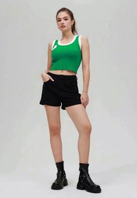 Top corto verde a coste con dettagli bianchi, abbinato a pantaloncini neri a vita alta e stivaletti neri con suola chunky.