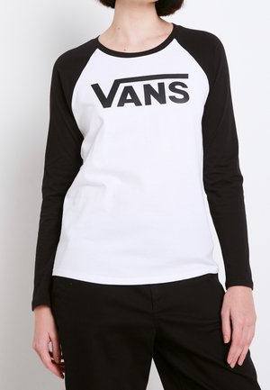 Osoba ubrana w białą i czarną raglanową koszulkę z długim rękawem z logo „VANS” na piersi oraz czarne spodnie, stojąca na jednolitym tle.