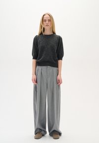 Dunkelgrauer, gestrickter Kurzarmpullover kombiniert mit lockeren, hellgrauen, plissierten Hosen. Modell trägt hellbraune Slipper.