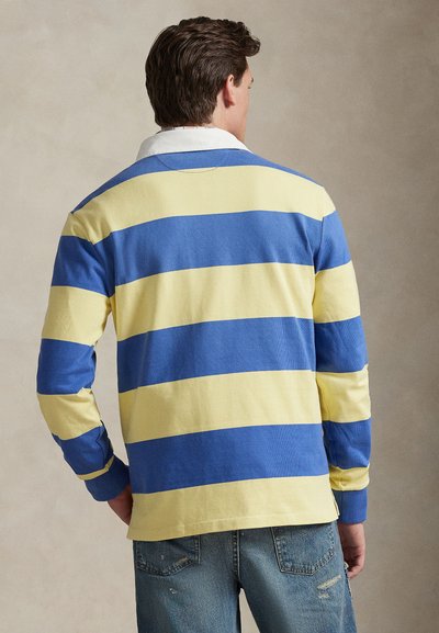 Μακρυμάνικο πόλο μπλουζάκι με οριζόντιες ρίγες σε μπλε και κίτρινο, με λευκό γιακά και υφή υφάσματος, συνδυασμένο με τζιν παντελόνι.
