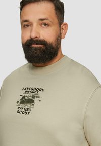 Sweatshirt beige en tissu texturé, avec un imprimé graphique noir d'un kayak et le texte "Lakeshore District Rafting Scout."