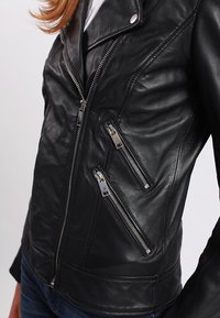 Black leather jacket with a fitted design, featuring multiple diagonal zippered pockets, silver hardware, and a textured finish.