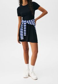 Czarna, prążkowana sukienka t-shirtowa z krótkimi rękawami, zestawiona z niebiesko-białym swetrem przewiązanym w talii oraz białymi sneakersami.
