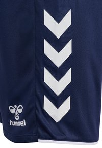 Shorts de sport bleu marine avec des rayures en forme de chevron blanches sur le côté et un logo hummel blanc près de l'ourlet.