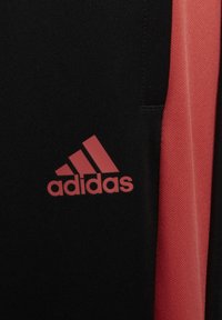 Adidas kledingstuk gemaakt van zwart en koraal kleurige stof met een zachte textuur. Het logo is opvallend weergegeven in koraal op het zwarte materiaal.