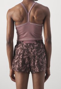 Reggiseno sportivo in rosa tenue con un design aderente, abbinato a pantaloncini marroni con un motivo floreale. Il materiale sembra liscio ed elastico.