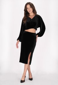 Zwarte fluwelen twee-delige outfit met een cropped top met volumineuze mouwen en een strak aansluitende rok met hoge split. Textuur met een gladde afwerking.