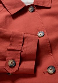 Rote Leinenjacke mit klassischem Kragen, großen Knöpfen mit Vierloch-Design und hochgekrempelten Ärmeln. Glatte Textur.