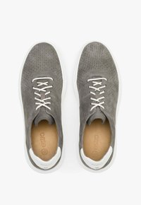Szare perforowane sneakersy z białymi sznurówkami, miękka skórzana tekstura, kontrastująca biała gumowa podeszwa i markowe wnętrze.