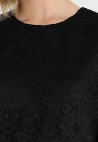 Top in pizzo nero con un motivo floreale e una finitura tessurizzata. Scollatura rotonda con maniche corte, che mette in evidenza dettagli intricatissimi.