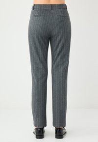 Graue, gestreifte Hosen mit schlanker Passform, ausgestattet mit einem Bund und zwei Gesäßtaschen, aus strukturiertem Stoff. Schwarze Schuhe runden den Look ab.